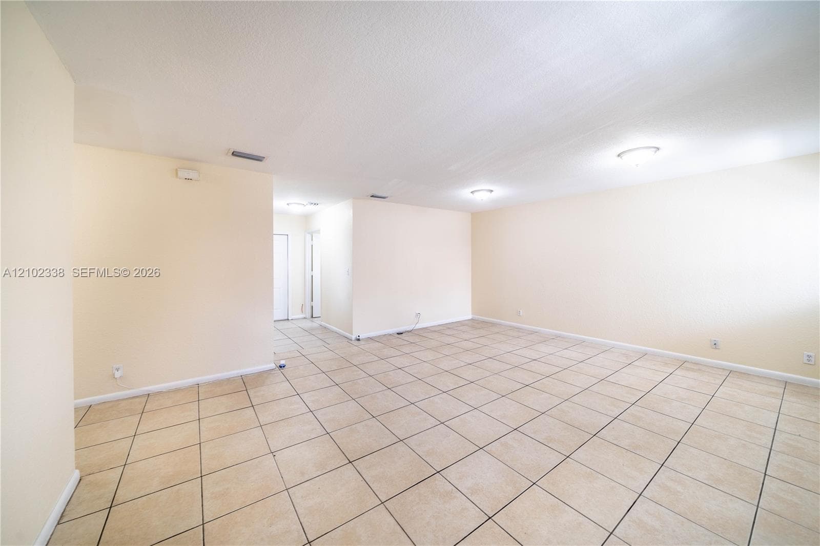 Expansive room featuring neutral-toned tile flooring, light-colored walls, and two ceiling-mounted light fixtures