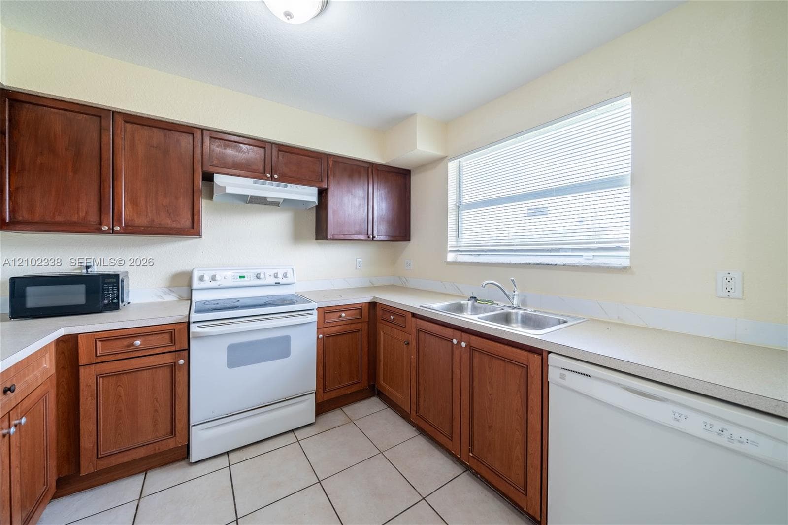 Kitchen featuring wood-finish cabinetry, solid surface countertops, a double basin sink, and a built-in dishwasher