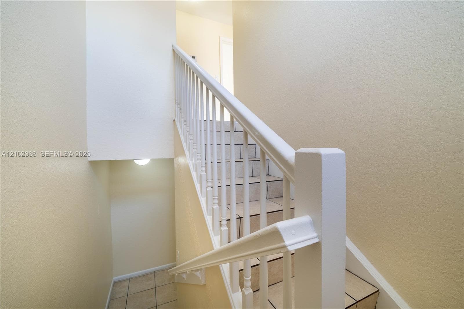 Staircase with white balusters, tile flooring at the base, and wall-mounted lighting