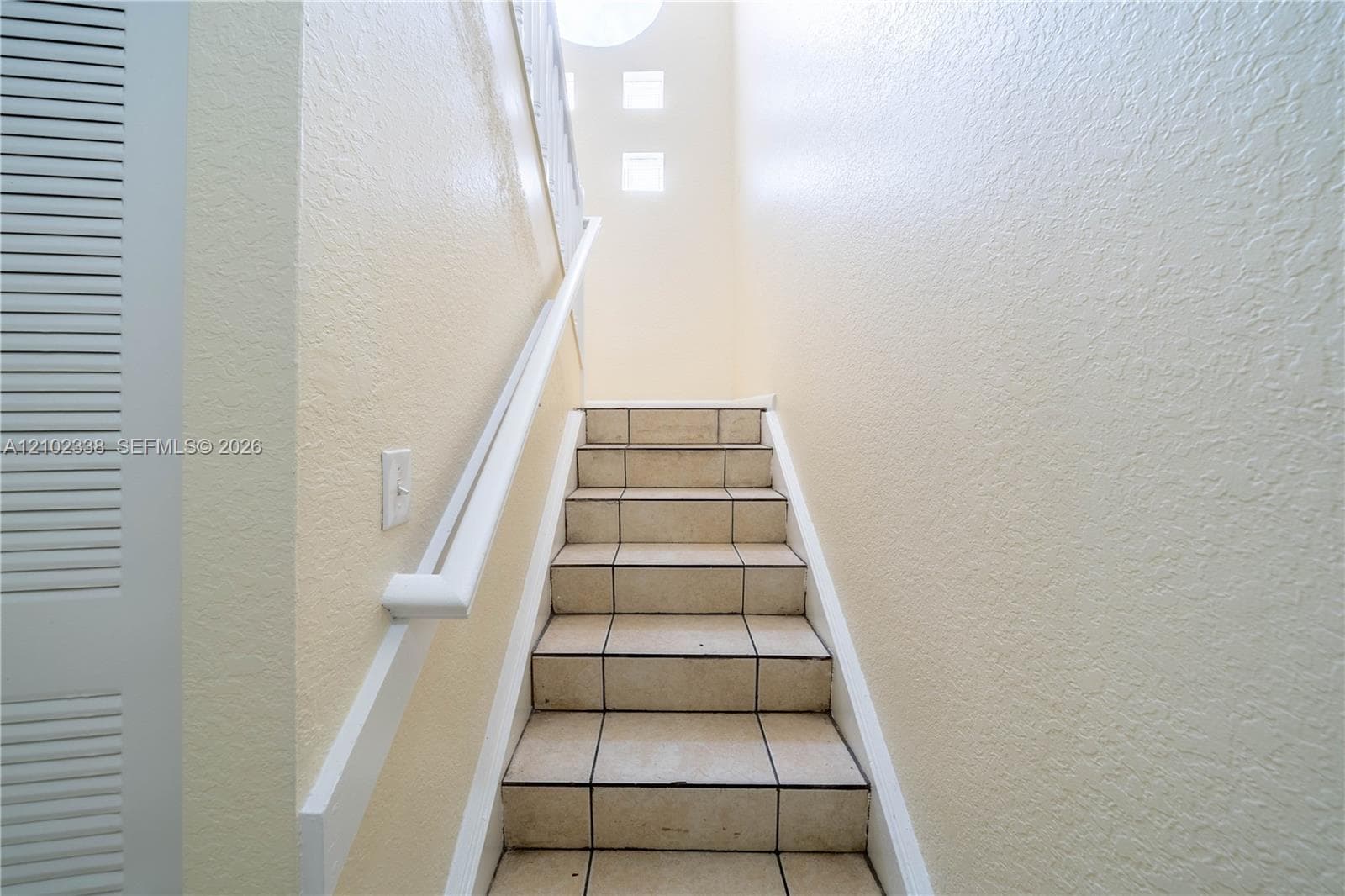 Staircase featuring tile treads, a white handrail, and textured wall finish