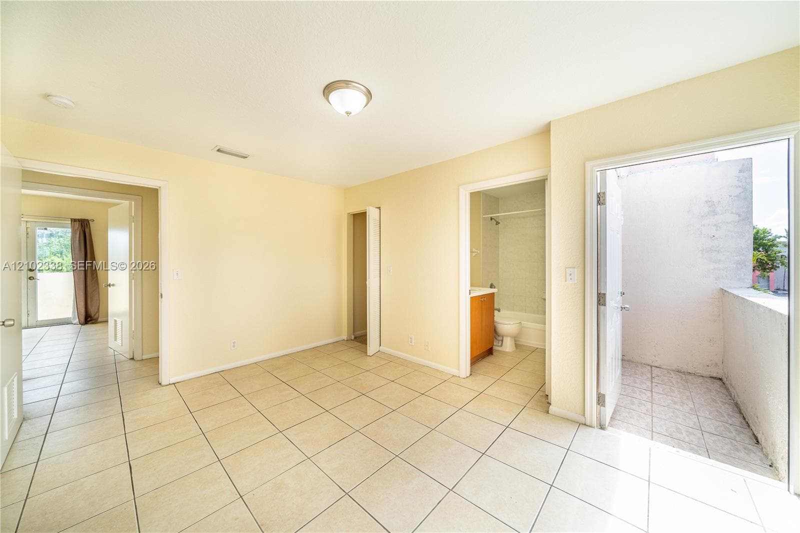 Tile flooring throughout, neutral wall tones, an overhead light fixture, and direct access to an outdoor balcony