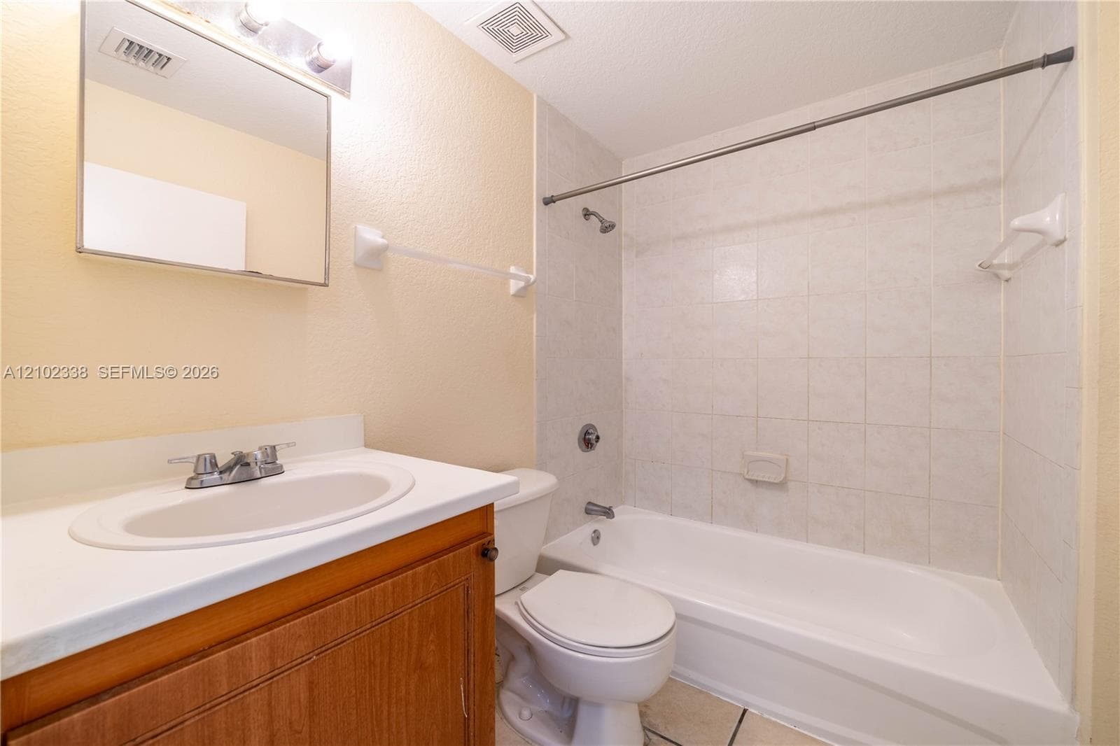 Bathroom featuring a wood-finish vanity with an integrated sink, a built-in bathtub, and ceramic tile flooring