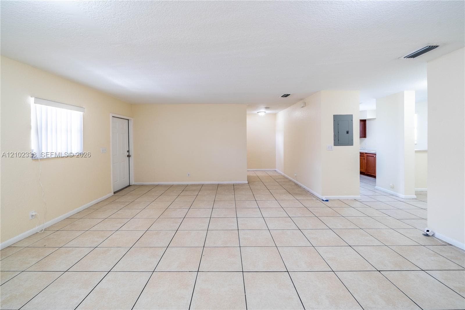 Expansive interior space featuring light-toned tile flooring, neutral wall finishes, and a window with vertical blinds