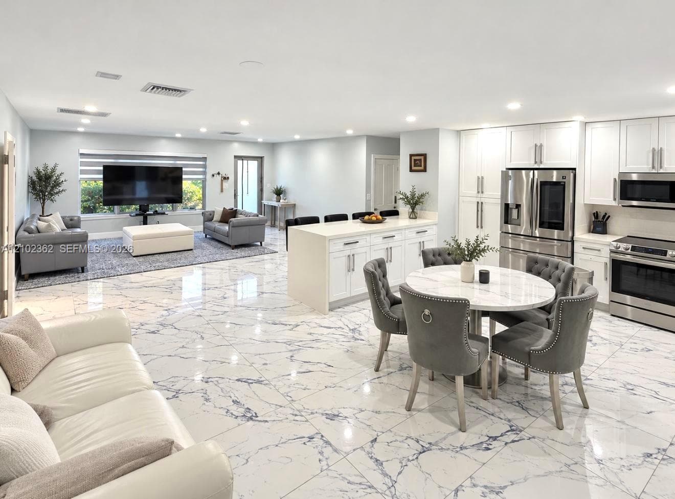 Large-format veined tile flooring, white cabinetry with silver-tone hardware, central kitchen island with cabinet storage, recessed lighting, and stainless steel kitchen appliances