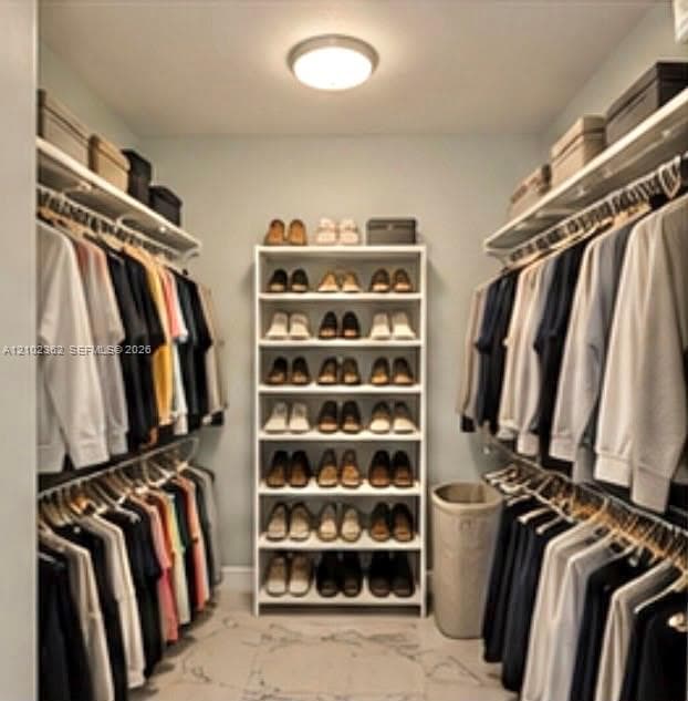 Walk-in closet featuring white built-in shelving, dual tiered hanging rods, and stone-finish flooring