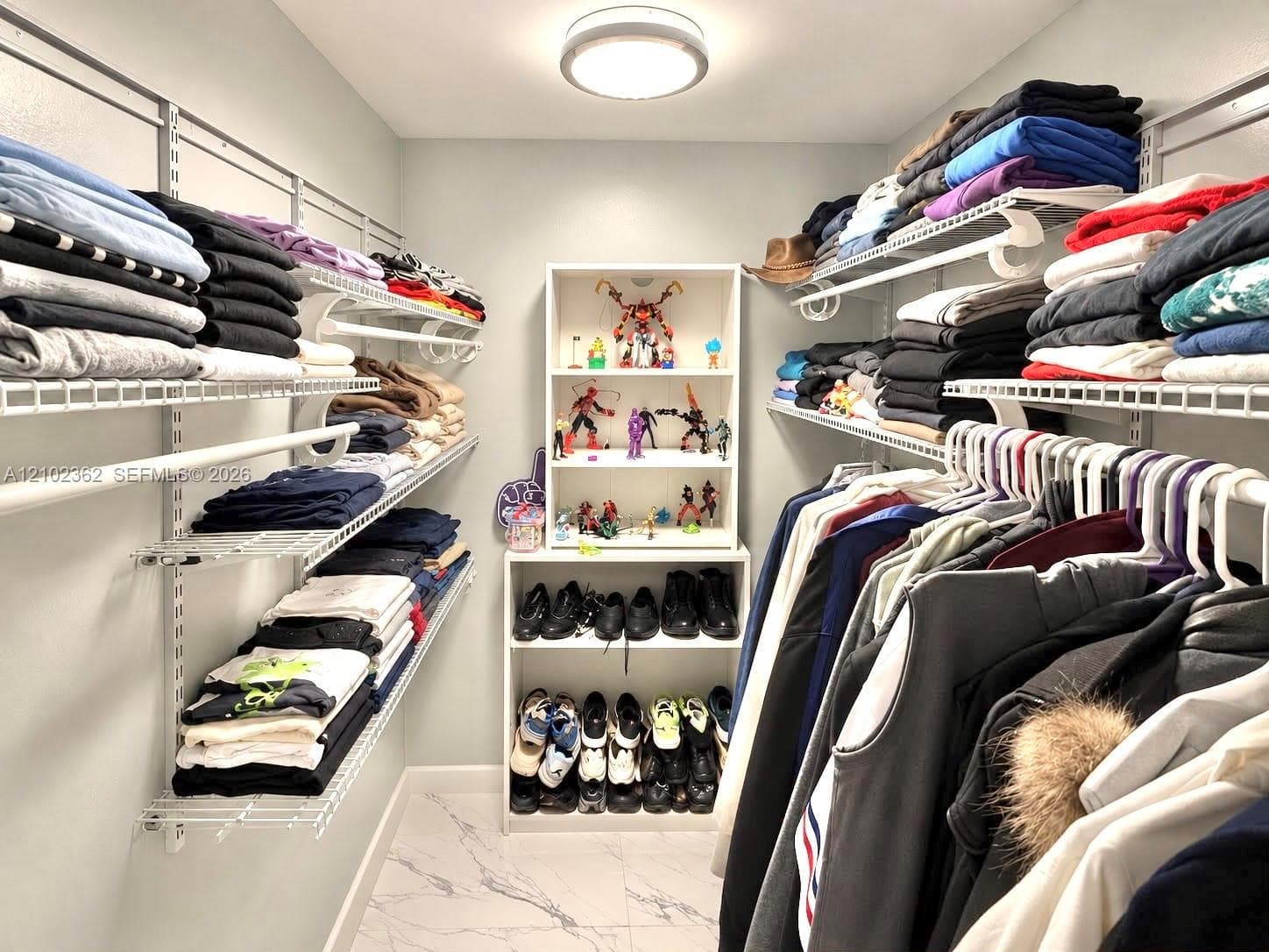 Walk-in closet featuring white wire shelving, adjustable hanging rods, built-in floor-to-ceiling cabinetry, and stone-finish tile flooring