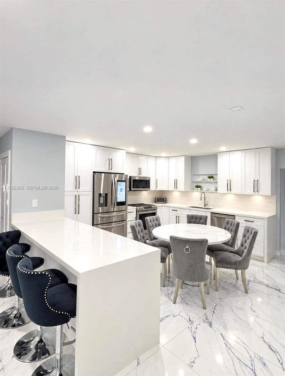 Kitchen featuring white cabinetry, quartz countertops, a waterfall-edge island, stainless steel appliances, and large-format tile flooring with marble-pattern veining
