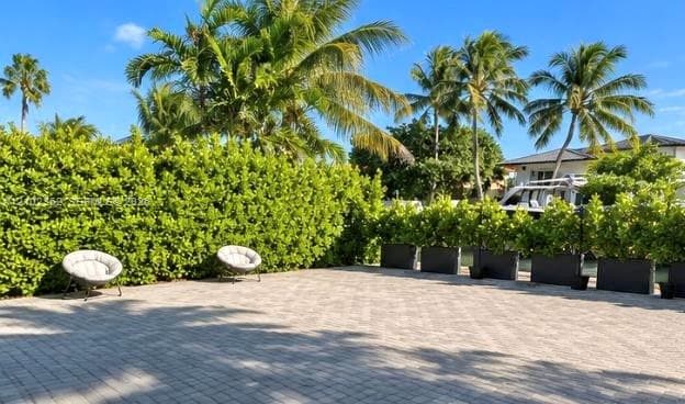 Paver patio featuring integrated perimeter hedging, mature palm trees, and dark-toned modular planters