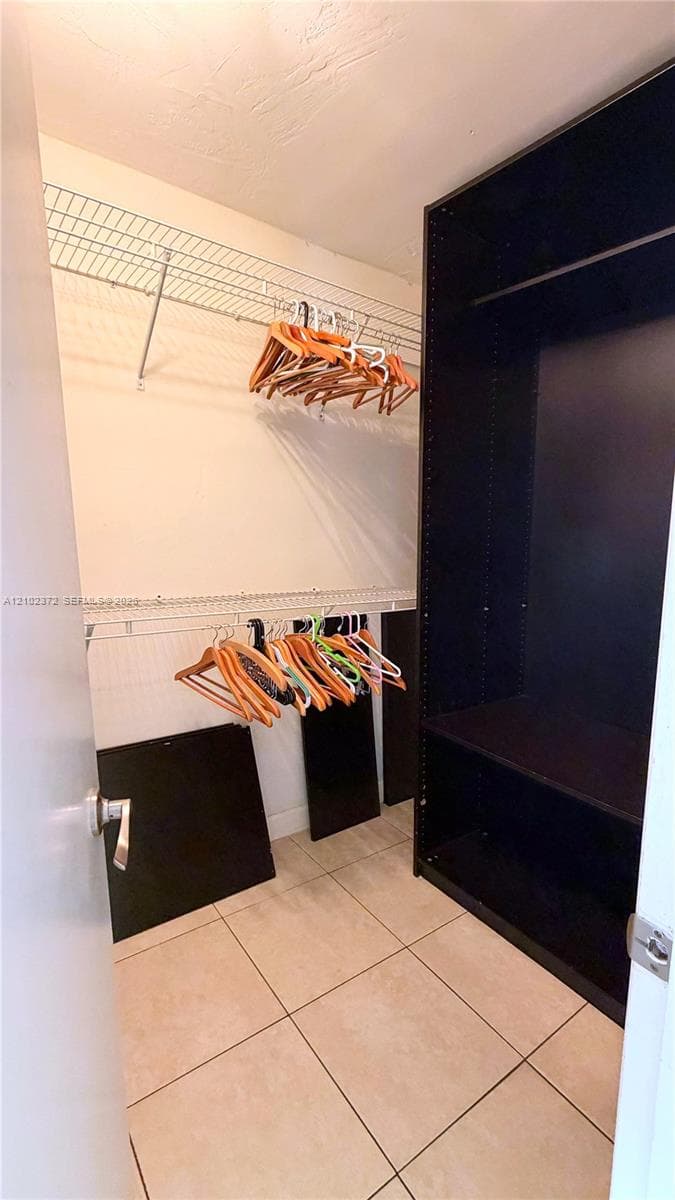 Walk-in storage space featuring ceramic tile flooring, built-in floor-to-ceiling shelving, and wire hanging racks