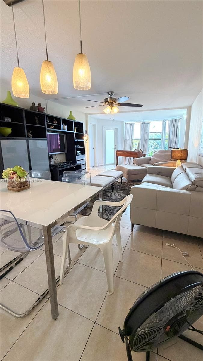 Open living area featuring neutral-tone ceramic tile flooring, built-in shelving unit, three glass pendant light fixtures, and a ceiling fan