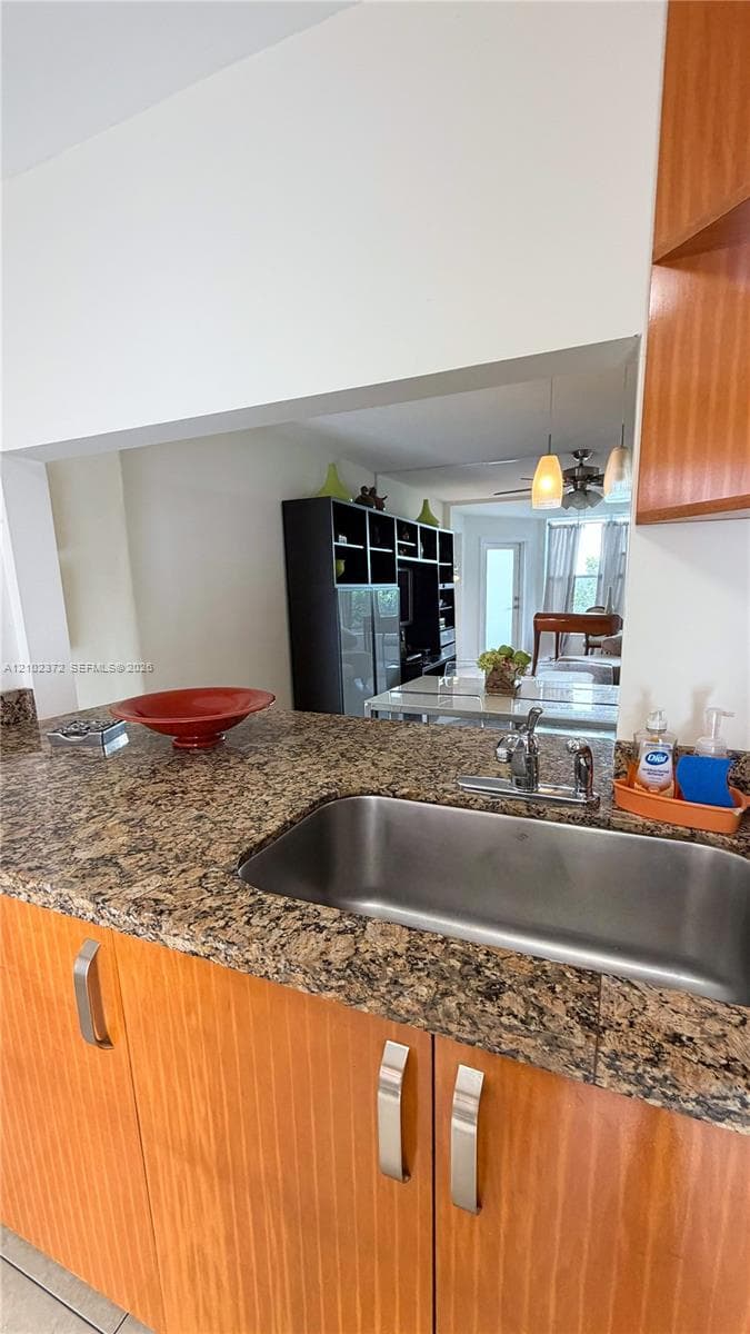 Kitchen featuring natural-finish wood cabinetry, stone-patterned countertops, a stainless steel undermount sink, and a high-arch chrome faucet