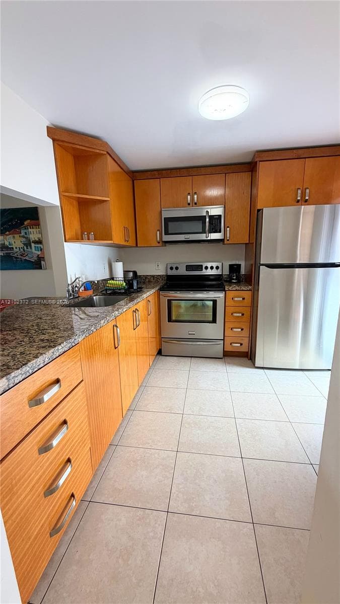 Kitchen featuring wood cabinetry, stone-finish countertops, tile flooring, and stainless steel appliances