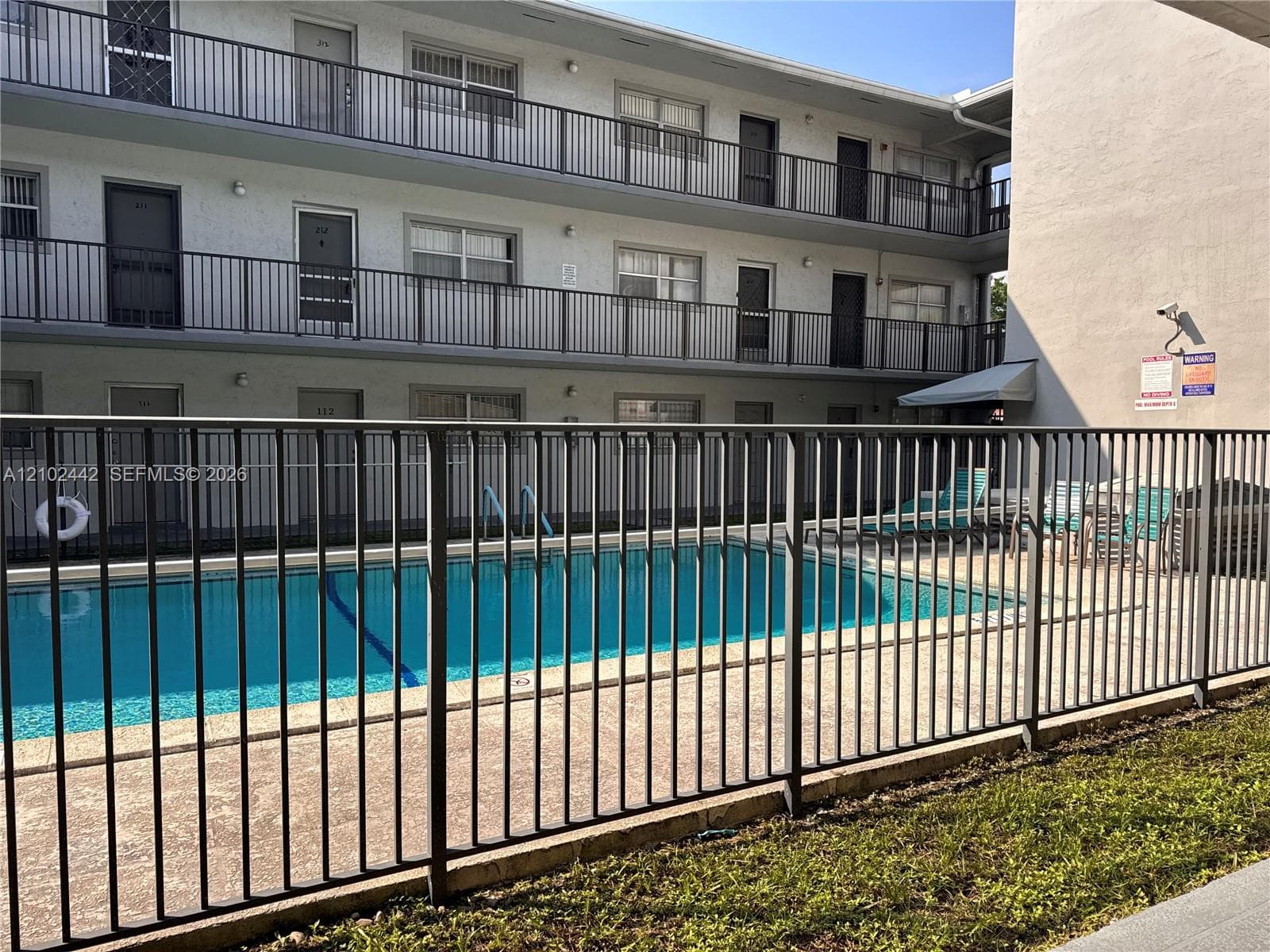 Enclosed swimming pool with a concrete deck, surrounded by a black metal fence