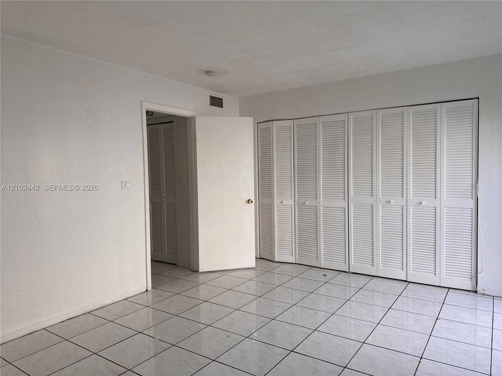 White interior walls with white bi-fold louvered closet doors, and white square tile flooring