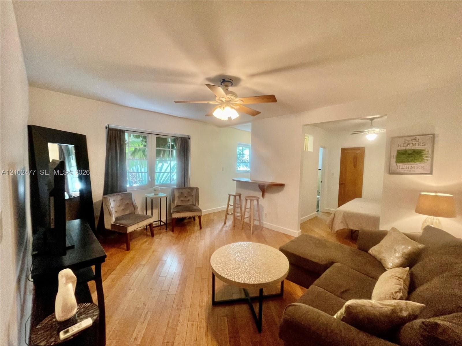 Living area featuring wood-finish flooring, a ceiling fan with integrated lighting, and a built-in wall-mounted breakfast bar