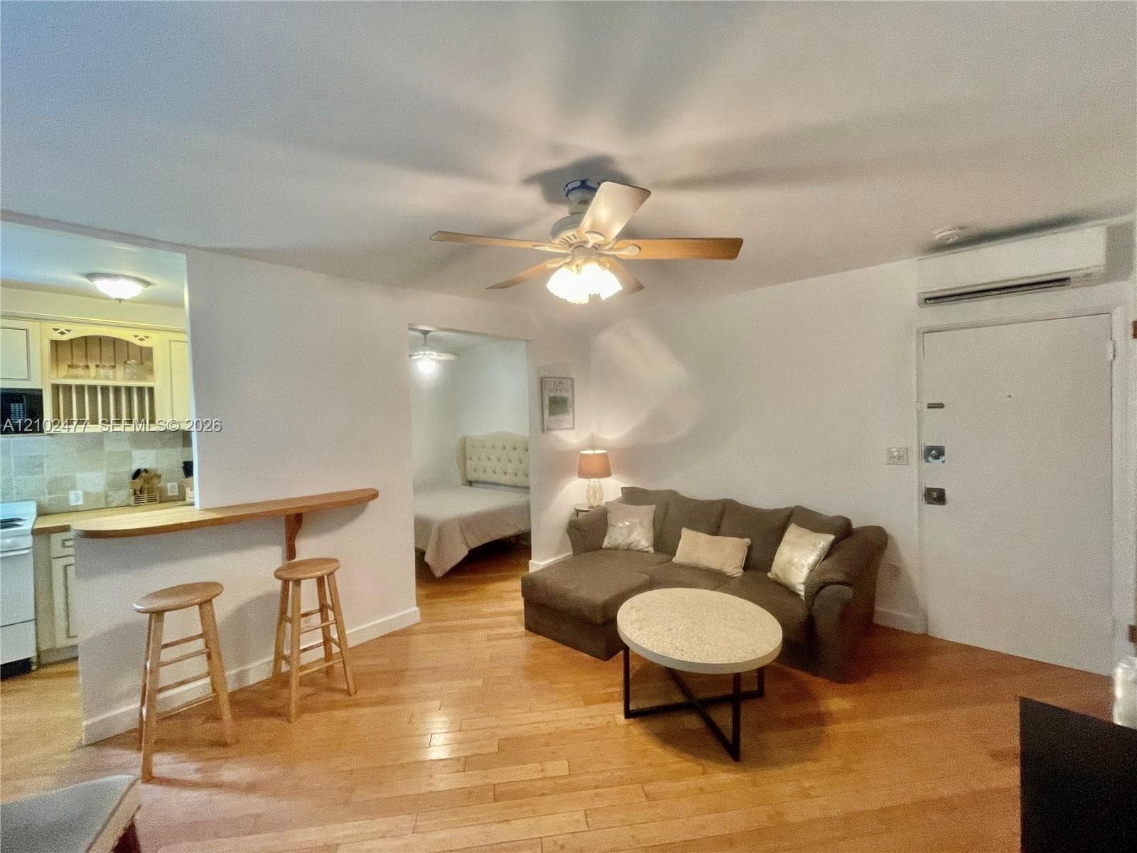 Open-concept area featuring wood-finish flooring, a breakfast bar, and a ceiling-mounted fan with integrated light fixture, complemented by a wall-mounted ductless heating and cooling unit