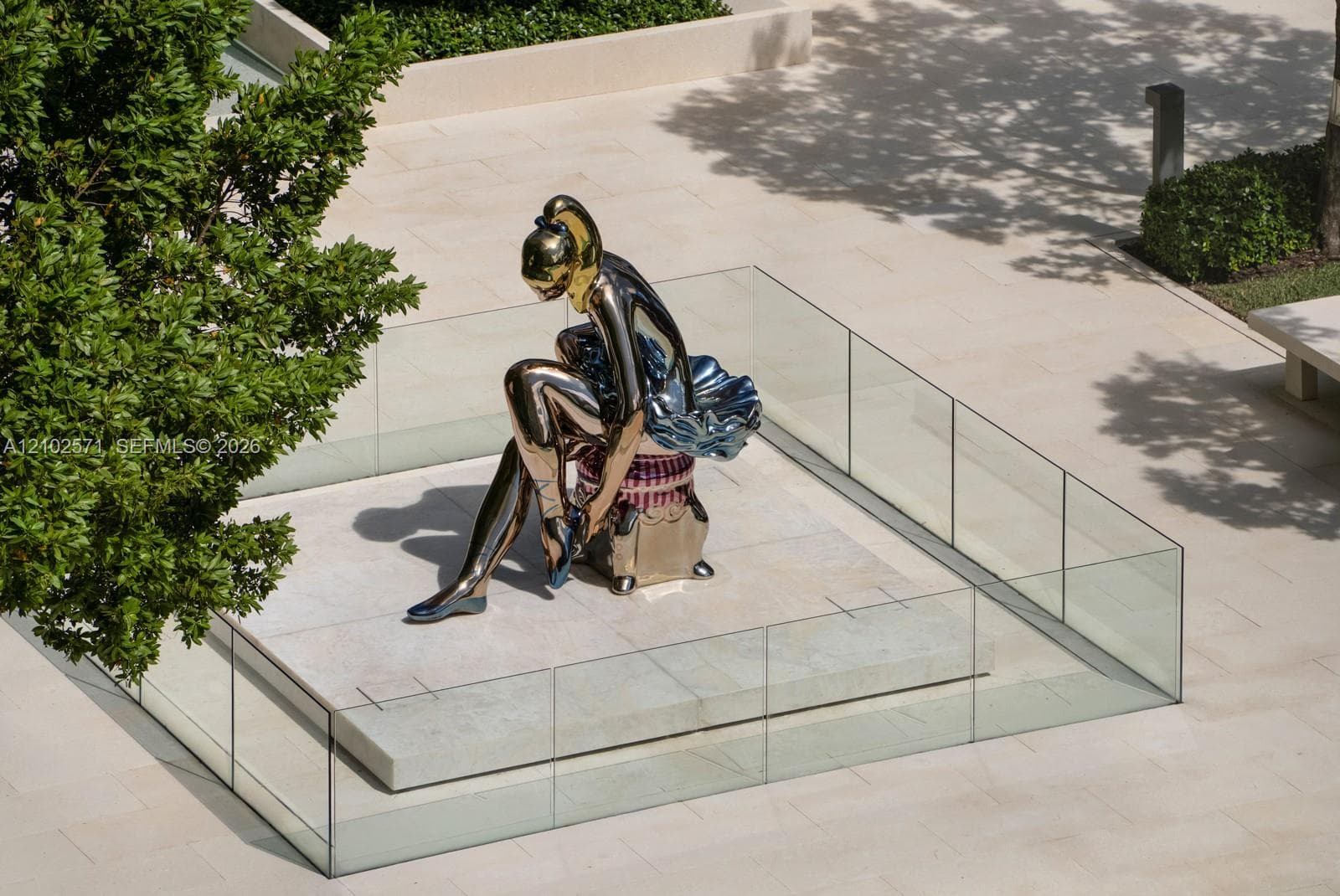 Communal courtyard featuring large-scale metallic sculpture, raised stone pedestal, perimeter glass railing, and smooth stone paving