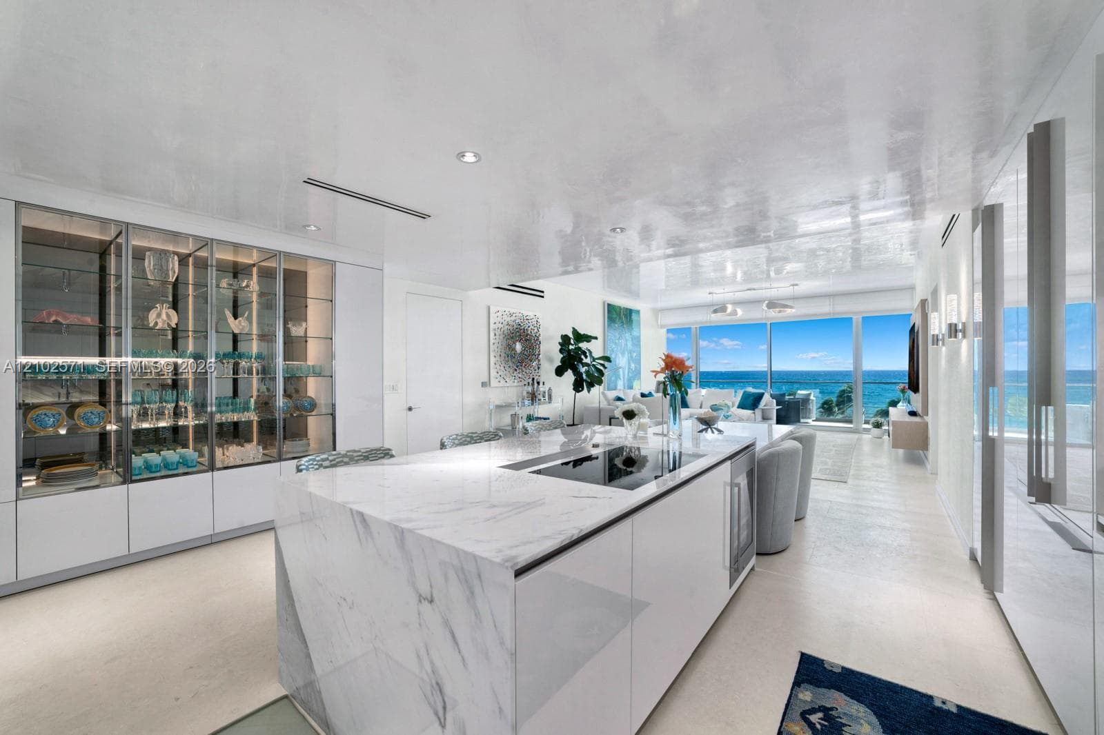 Kitchen island featuring a stone waterfall countertop with an integrated cooktop and under-counter beverage refrigeration, floor-to-ceiling glass-front cabinetry, polished finish ceiling, recessed lighting, and floor-to-ceiling glass doors opening to an ocean backdrop