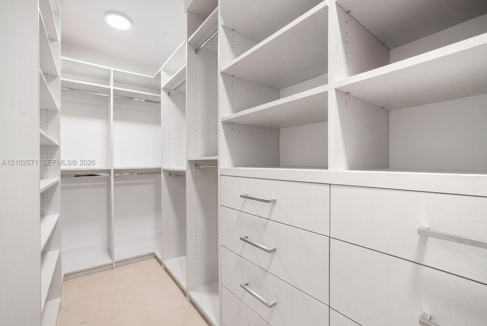 Walk-in closet featuring white custom cabinetry, adjustable shelving, integrated hanging rods, and built-in drawers with brushed nickel hardware
