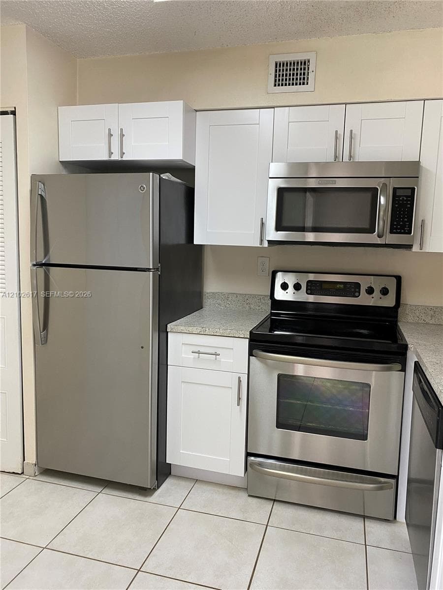 Kitchen featuring white shaker-style cabinetry, stone-finish countertops, and stainless steel appliances including a refrigerator, over-the-range microwave, and electric range