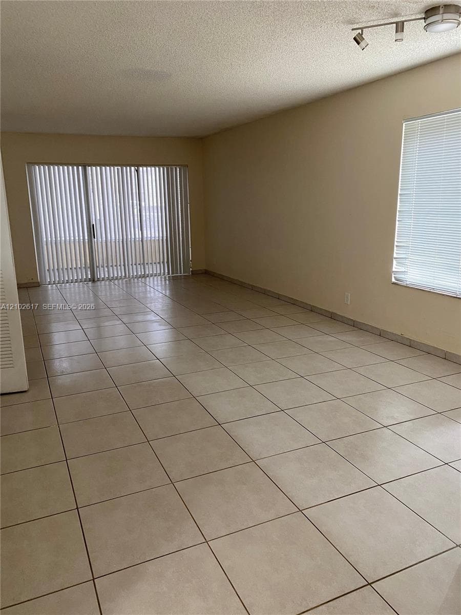Interior space featuring large-format tile flooring, multi-panel sliding glass door with vertical blinds, window with horizontal blinds, and ceiling-mounted track lighting