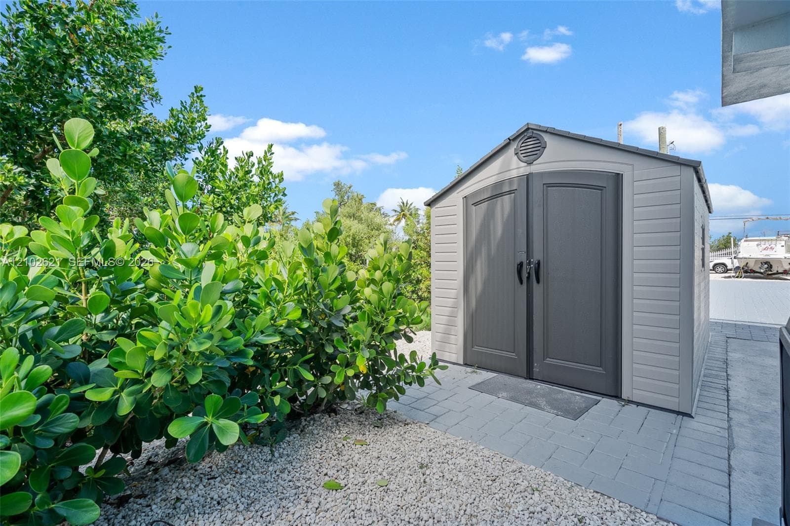 Storage shed with double doors, paved walkway, and lush perimeter landscaping
