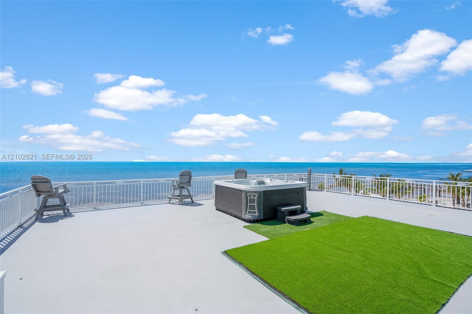 Rooftop deck featuring a hot tub, artificial turf area, and white perimeter railing
