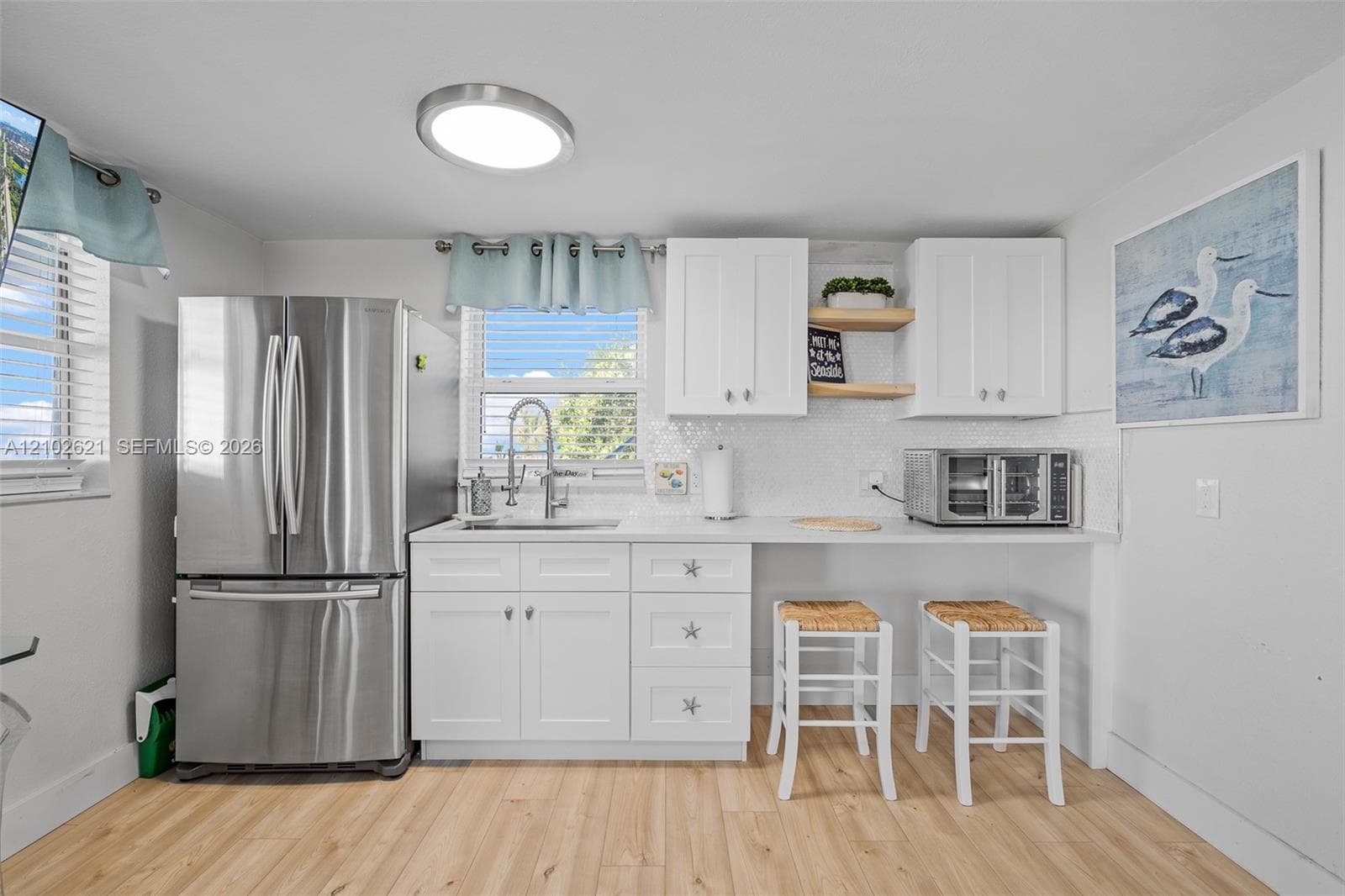 White cabinetry with stainless steel hardware, stainless steel refrigerator, white countertops, tile backsplash, and wood-finish flooring