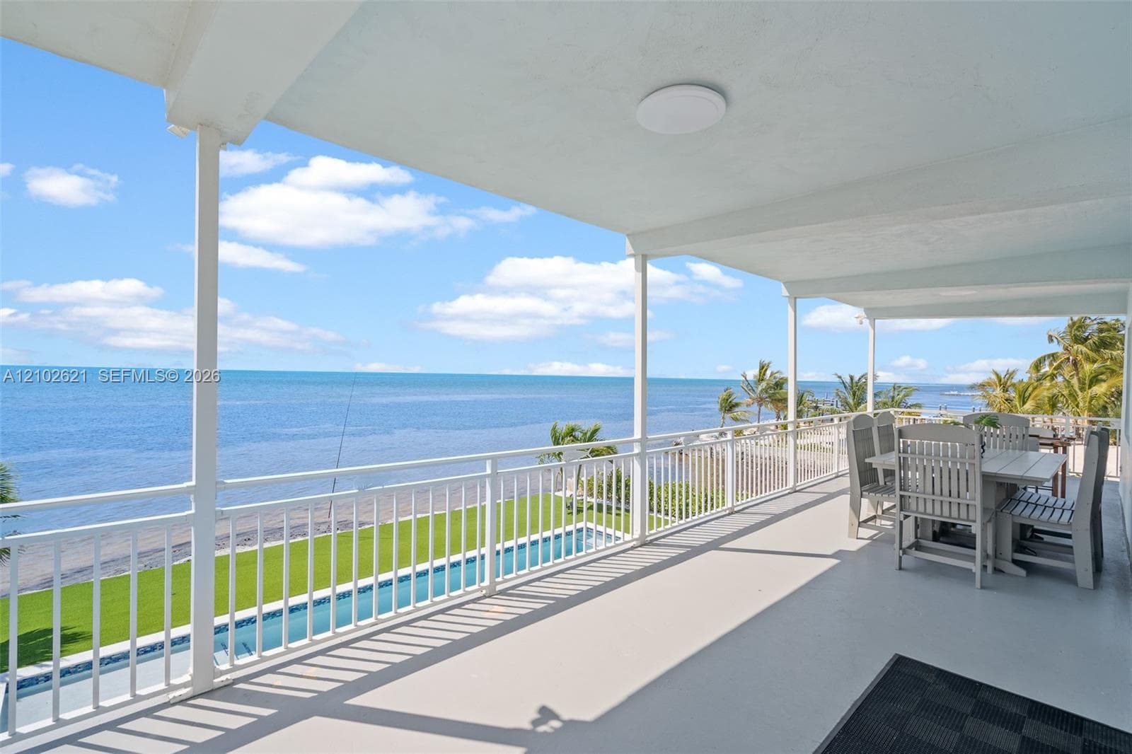 Expansive covered balcony featuring a coastal backdrop, white railing, outdoor ceiling light, and direct water exposure