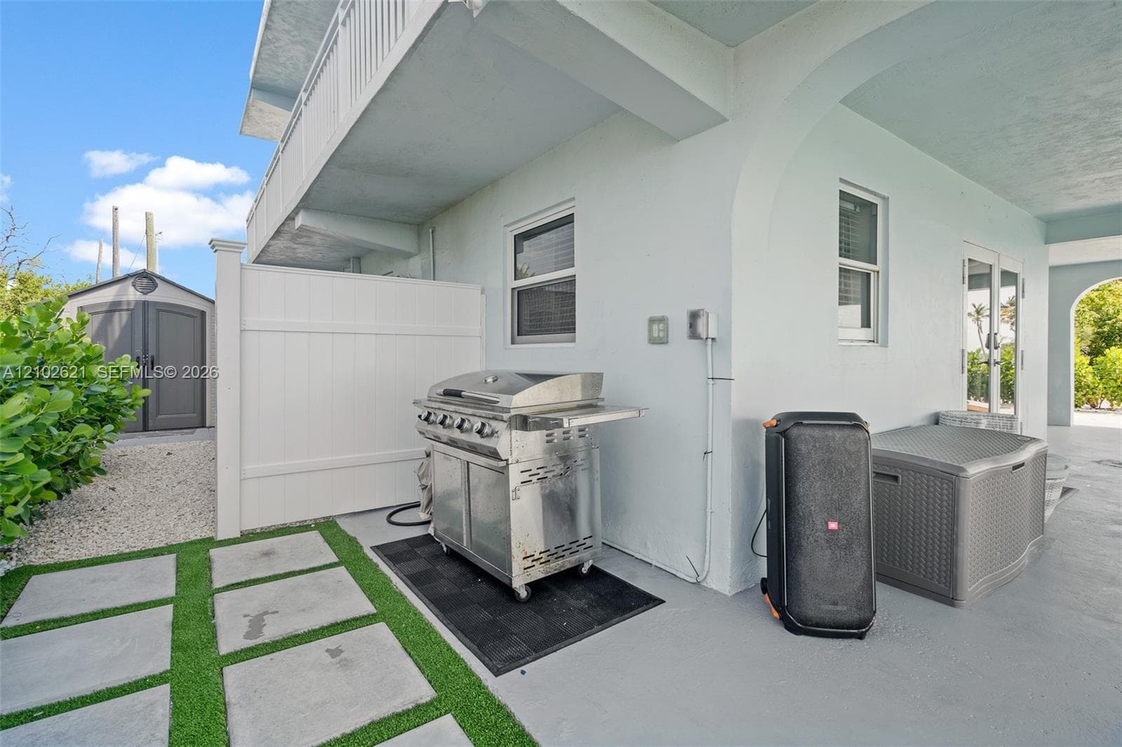 Covered patio area with concrete flooring, framed by arched entryways, featuring a white privacy fence and a built-in outdoor storage shed