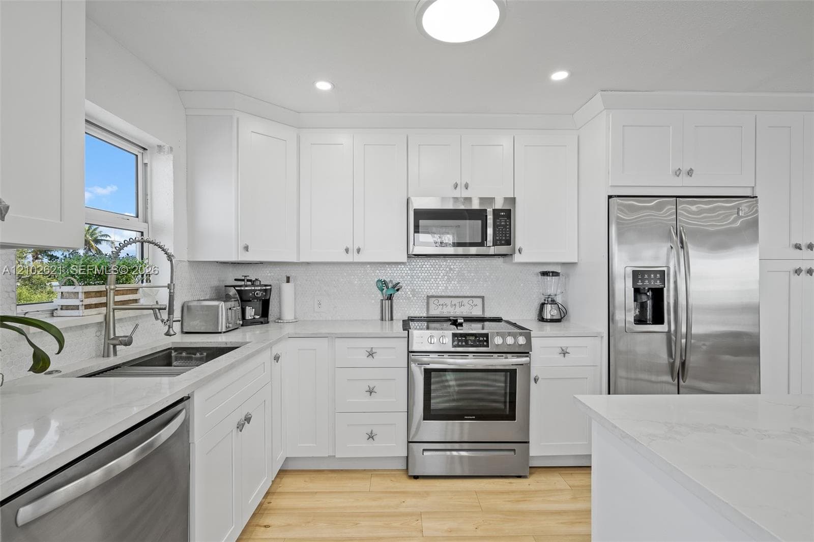 White shaker cabinetry, stainless steel appliances, light wood-finish flooring, white countertops, and a mosaic tile backsplash