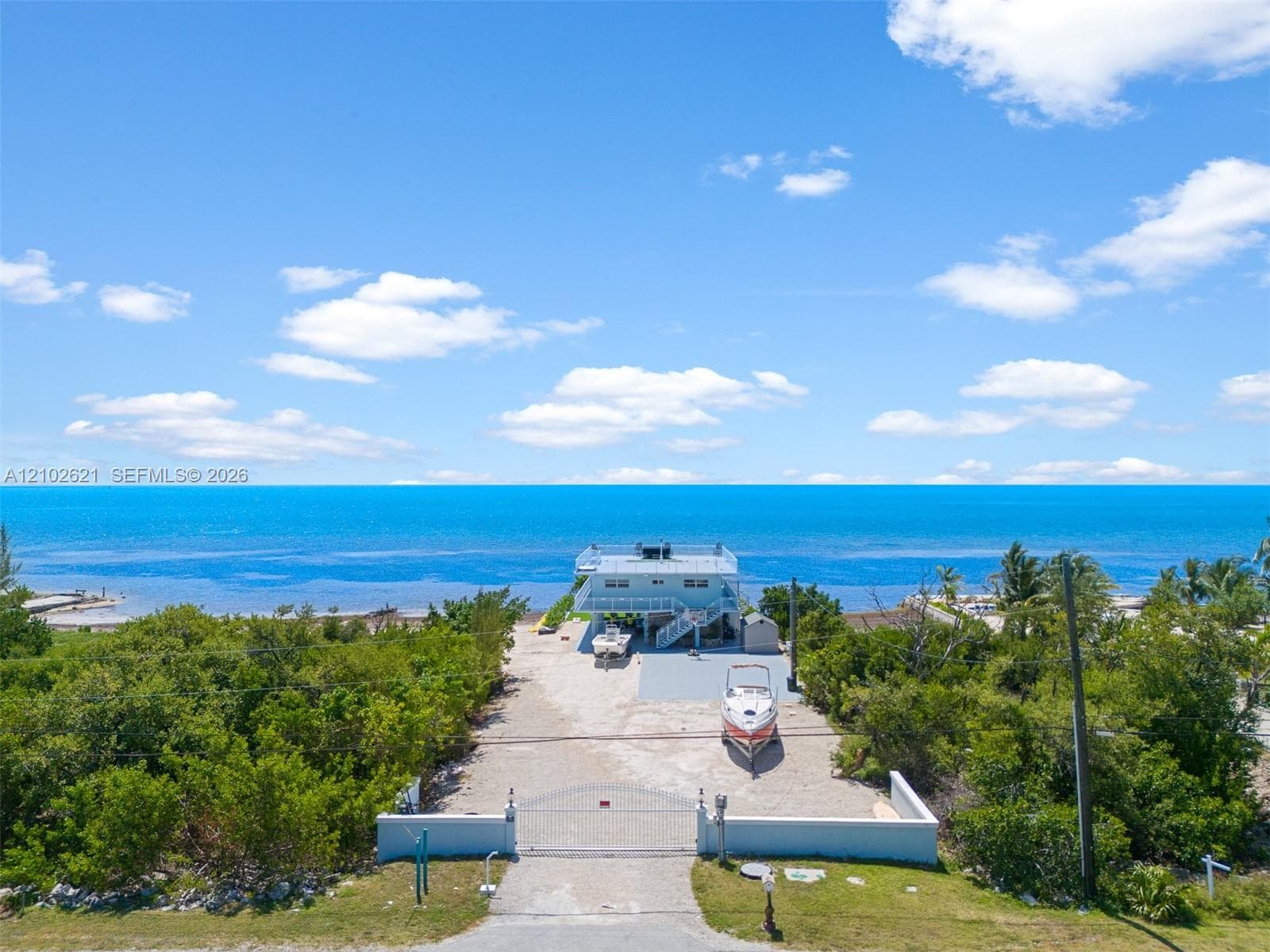 Waterfront property featuring a gated entrance, paved driveway, and lush surrounding foliage