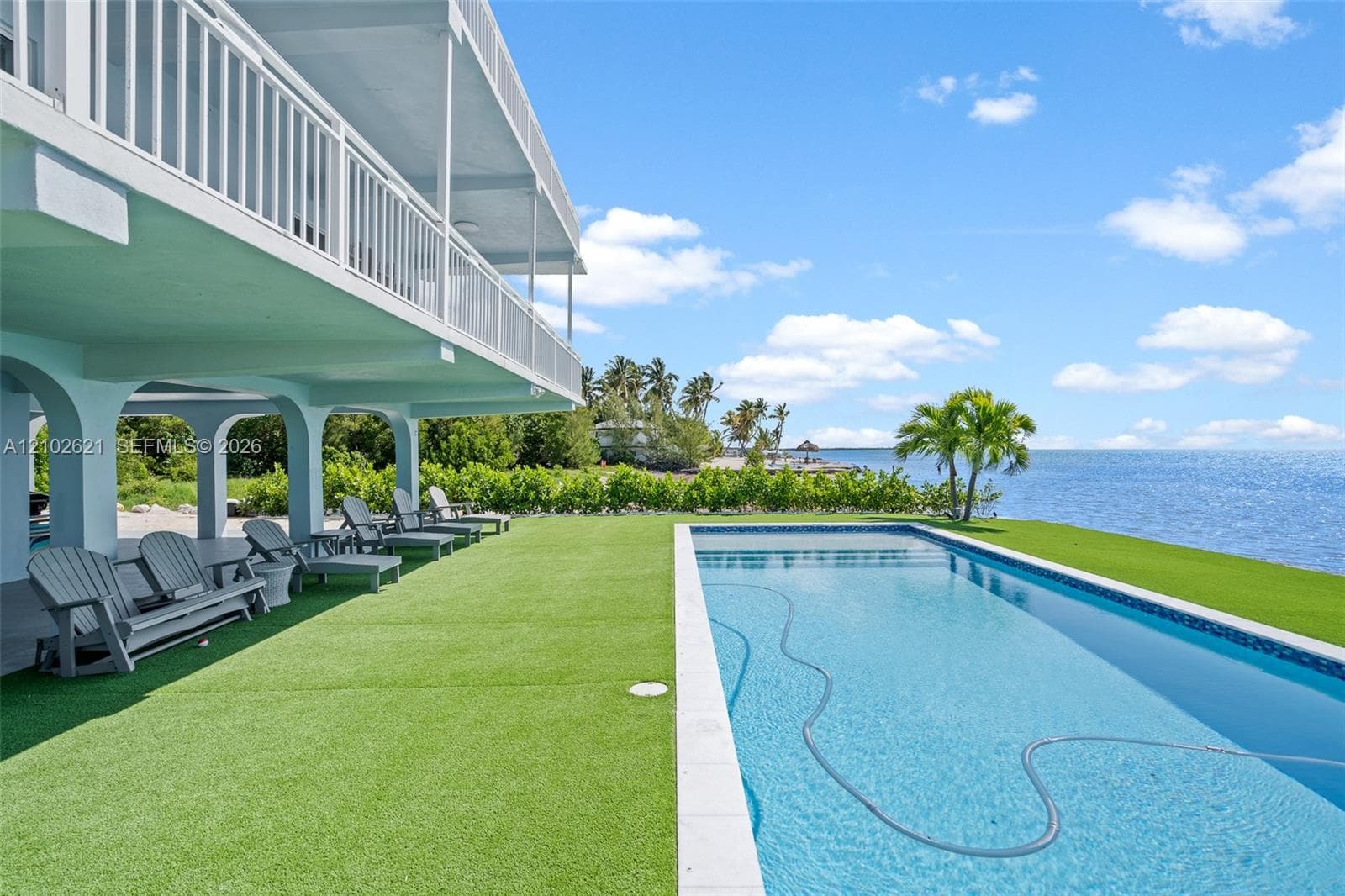 Waterfront property featuring a large swimming pool, expansive artificial turf lawn, and an elevated balcony with white railings
