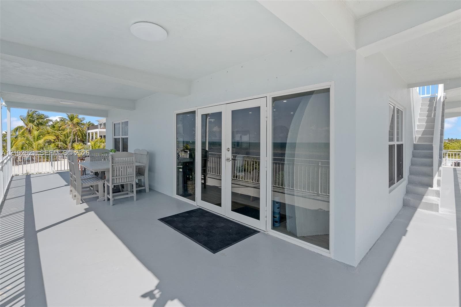 Expansive covered balcony with a white railing, large glass doors, and exterior staircase access