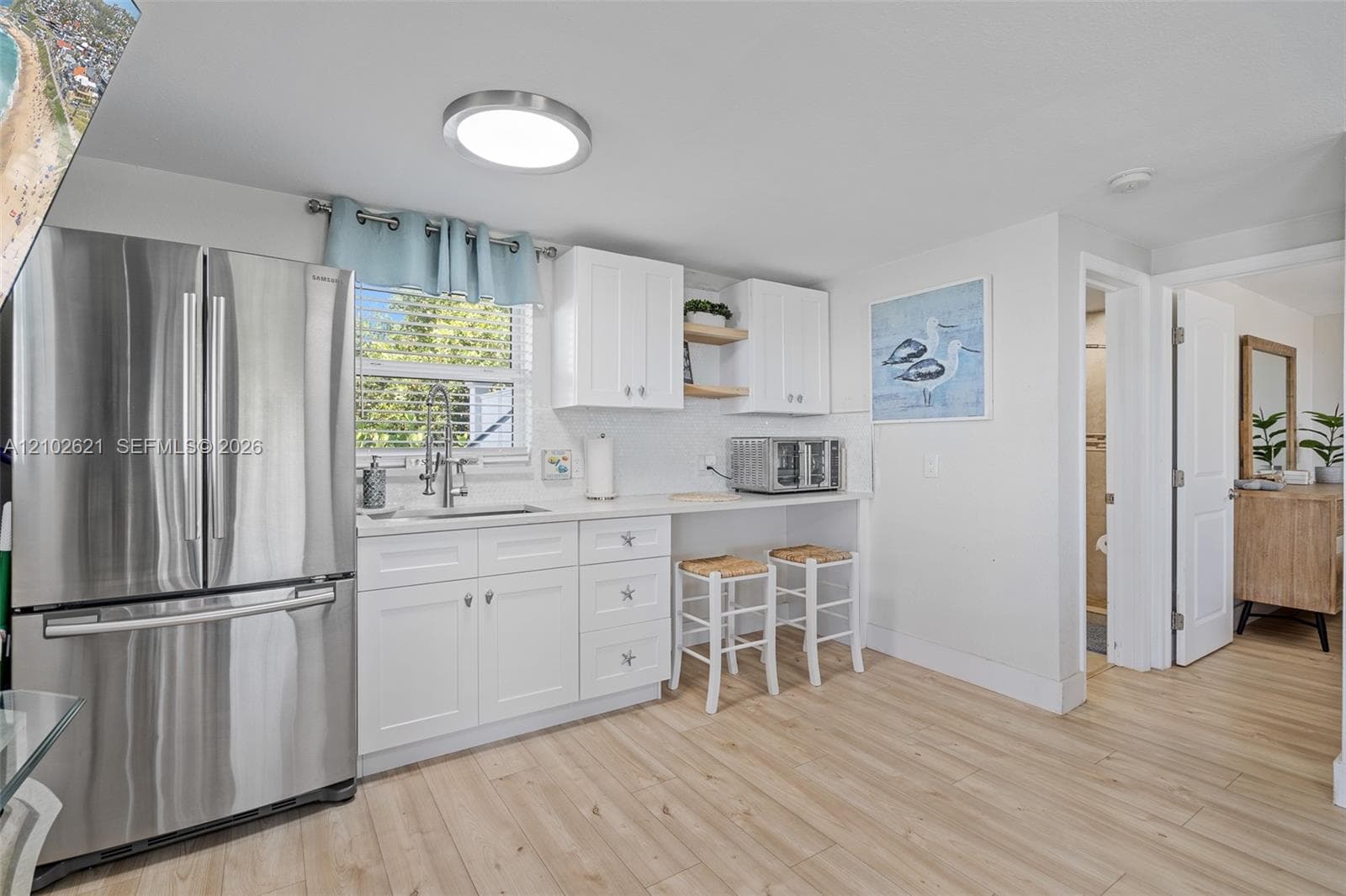 Stainless steel refrigerator, white cabinetry, wood-finish flooring, recessed lighting, and a window with natural light