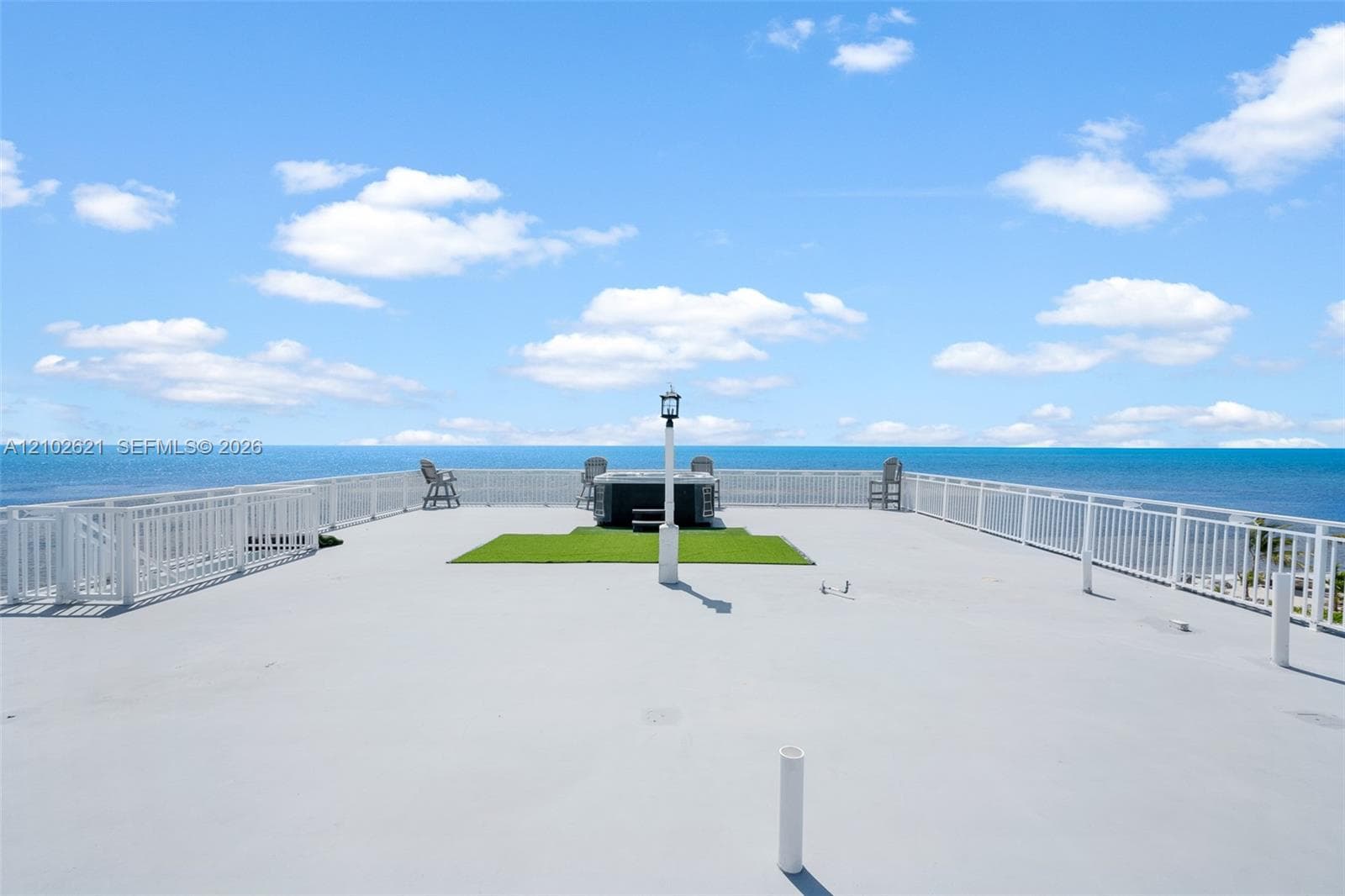 Expansive rooftop deck featuring a hot tub, artificial turf area, and perimeter white railings