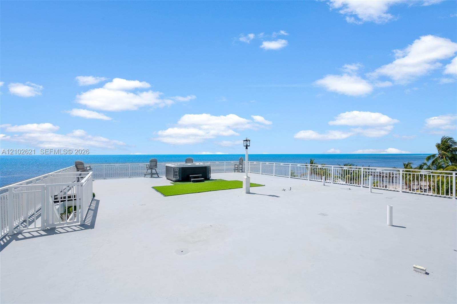 Rooftop deck featuring a hot tub, artificial turf accent, white railings, and a security gate