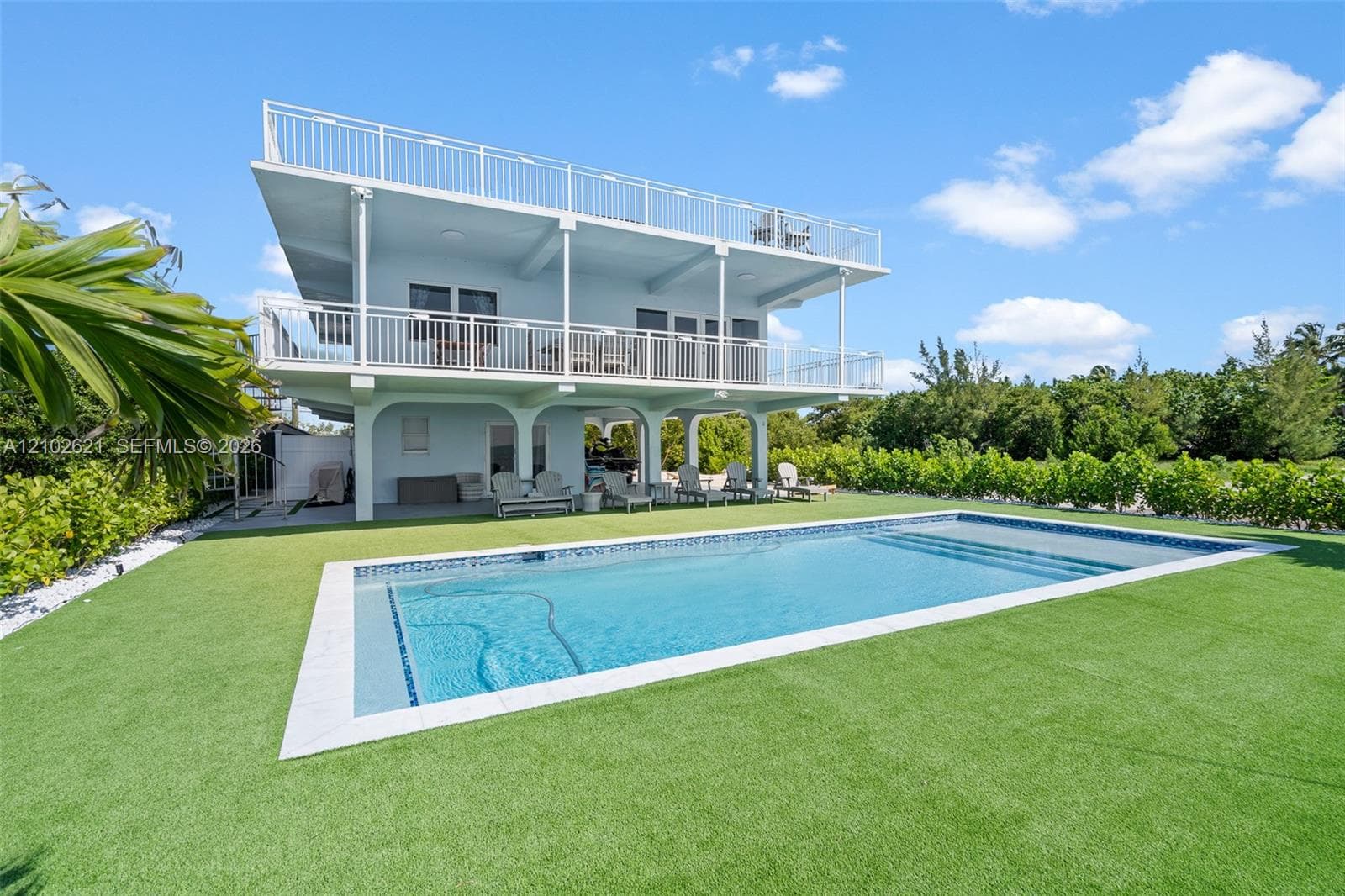 Elevated home featuring multiple balconies, a rooftop deck, an in-ground swimming pool, and a manicured artificial turf lawn