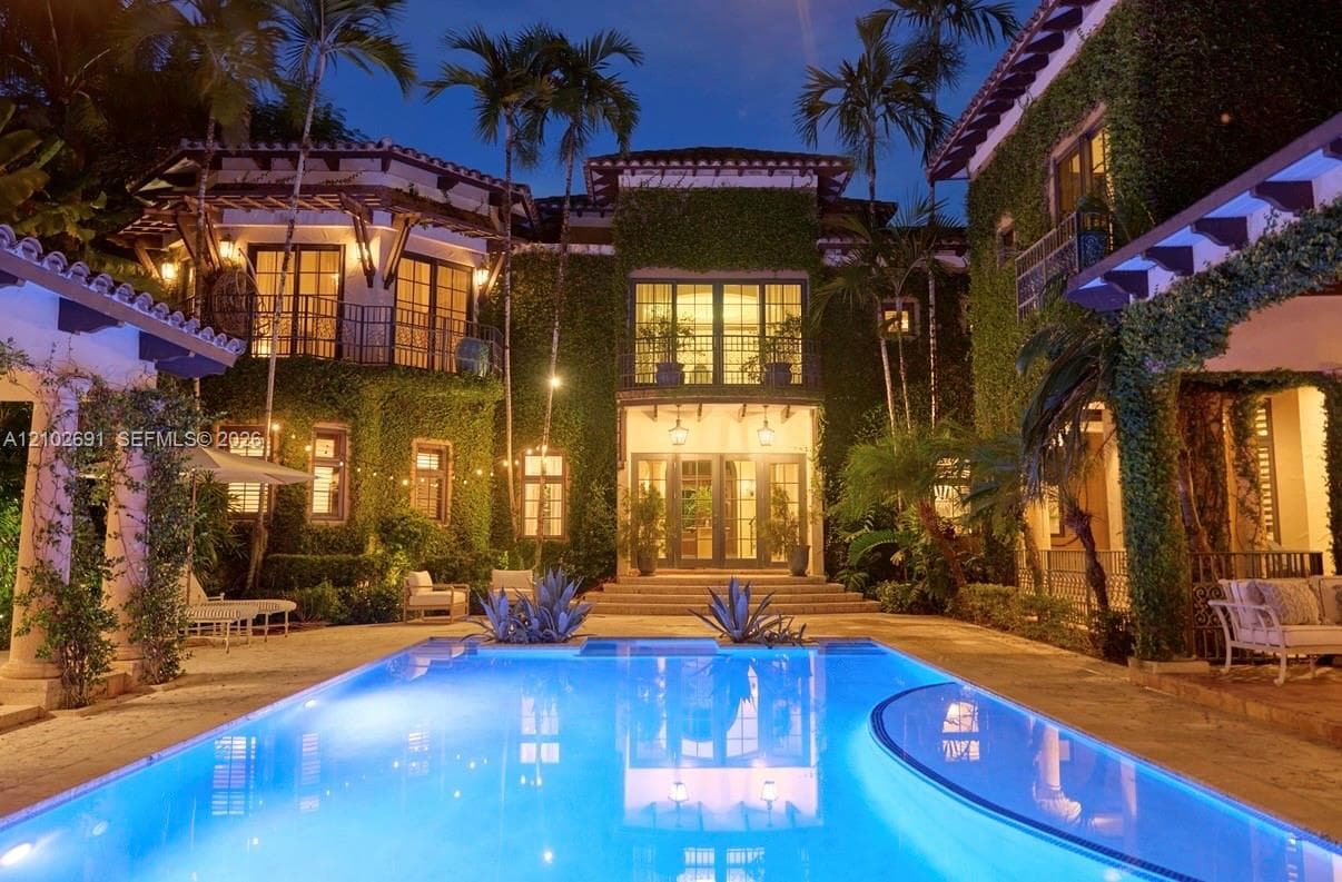Mediterranean-style estate featuring an ivy-clad exterior, multi-level balconies, stone-paved patio, and a rectangular in-ground swimming pool with an integrated spa