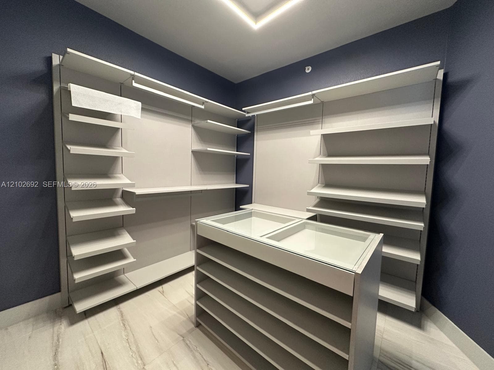 Custom storage system featuring adjustable shelving, integrated linear lighting, a central display island with a glass top, and stone-finish flooring