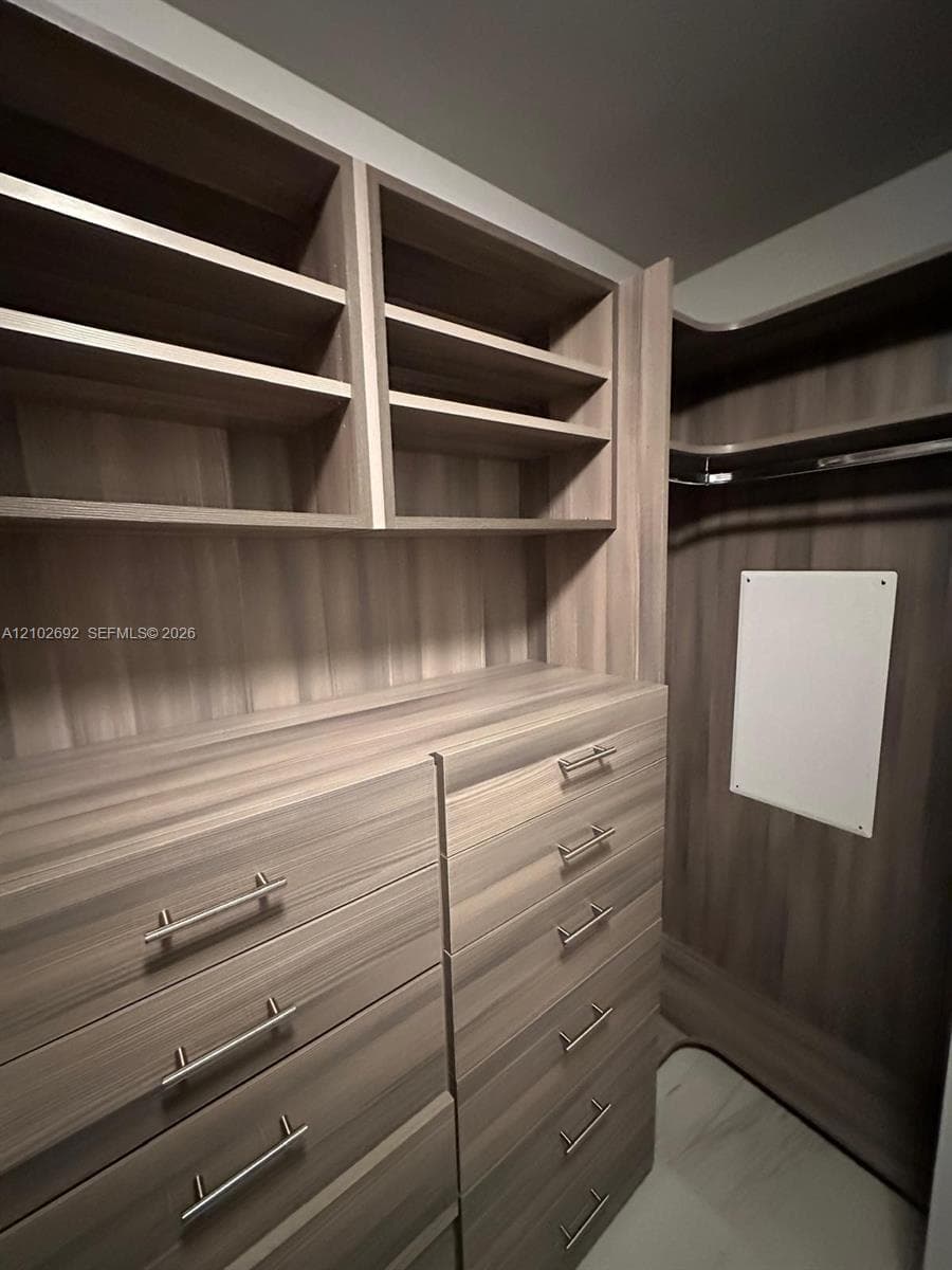 Built-in closet system featuring wood-finish cabinetry, multi-tier open shelving, integrated dresser drawers, brushed metal hardware, and a hanging rod