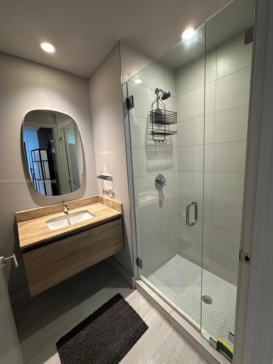 Floating vanity with wood-finish cabinetry, rectangular under-mount sink, frameless glass shower enclosure, and tiled shower surround with mosaic floor tiling