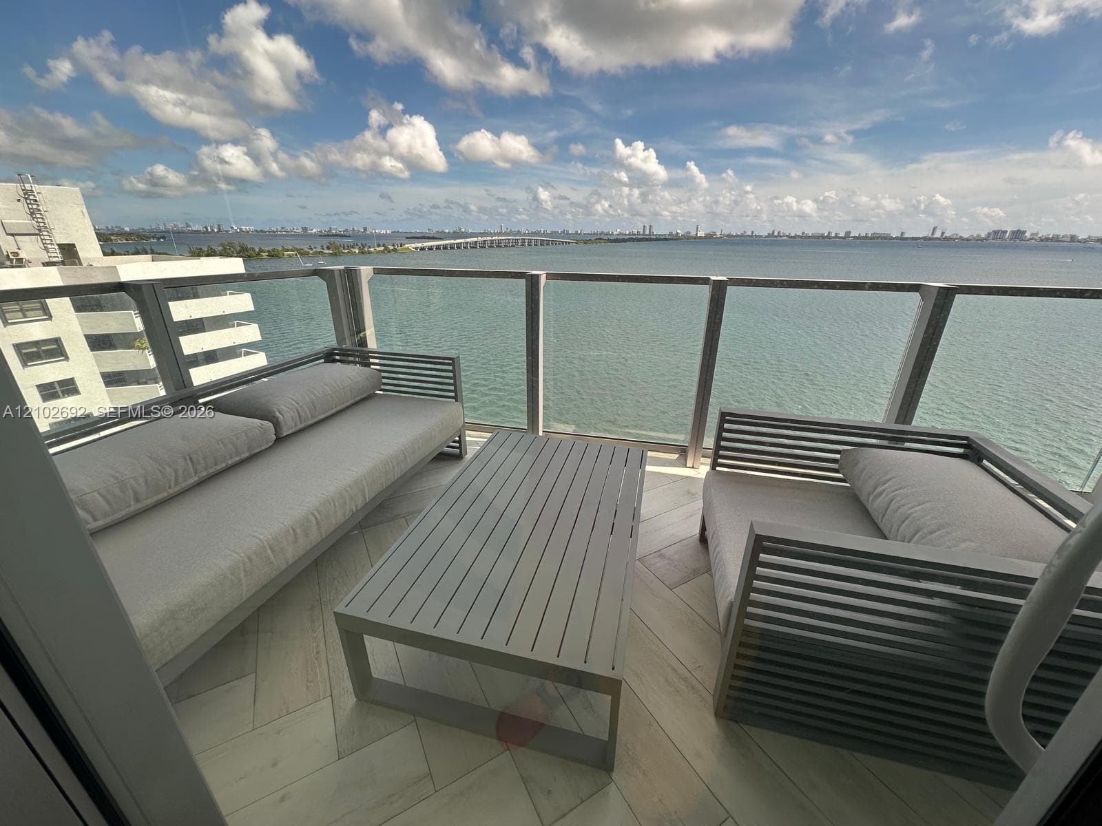 Private balcony featuring herringbone-patterned tile flooring and a glass-paneled railing overlooking the water