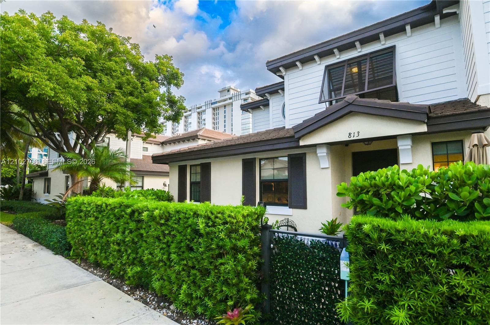 Multi-story exterior featuring lap siding, decorative shutters, a covered entryway, and landscaped hedging
