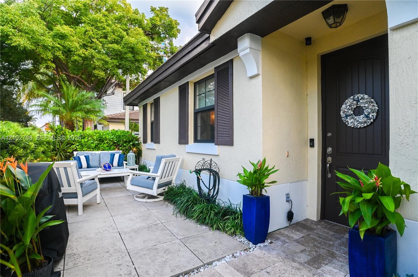 Stucco exterior featuring dark brown shutters, a solid-paneled front door, stone-tile patio flooring, and decorative corbel accents