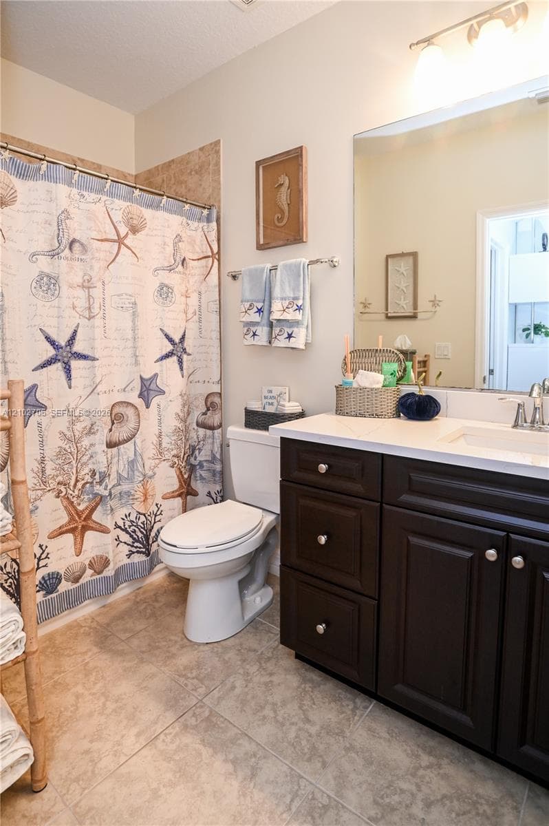 Dark-finish cabinetry, solid-surface countertop with an integrated basin, large-format tile flooring, and a full-width vanity mirror