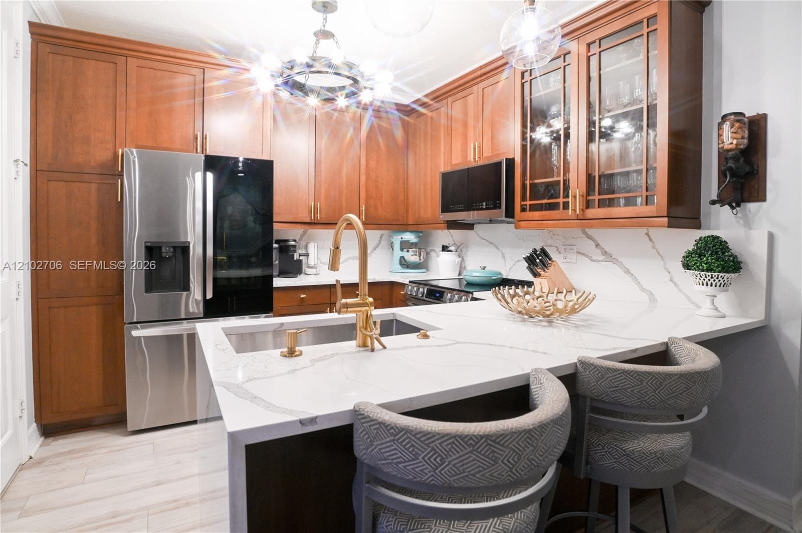 Kitchen featuring wood cabinetry, stone-surface countertops, stainless steel appliances, a brass-finish faucet, and overhead statement lighting