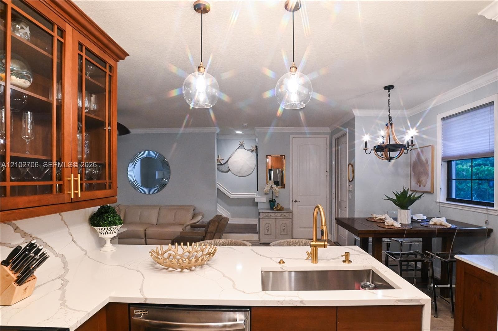 Kitchen featuring quartz countertops, wood-finish cabinetry, stainless steel undermount sink, brass-tone hardware, and glass pendant lighting