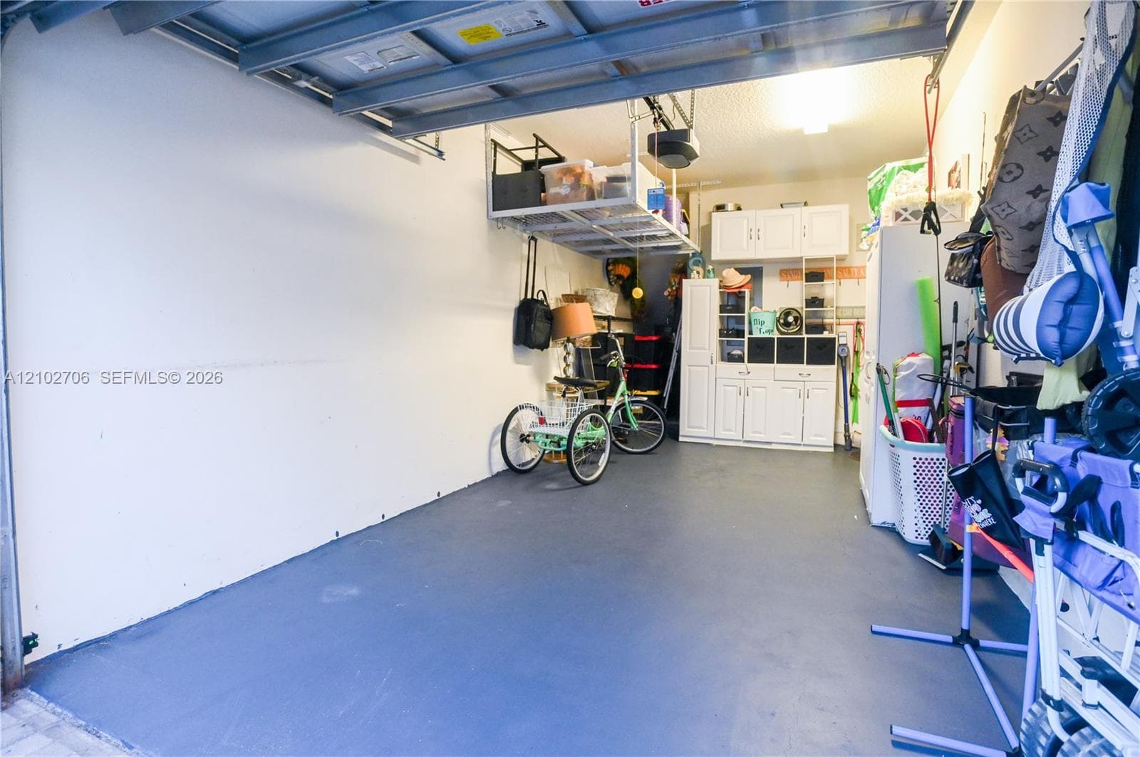 Garage featuring a painted floor surface, built-in white cabinetry, and overhead storage racking
