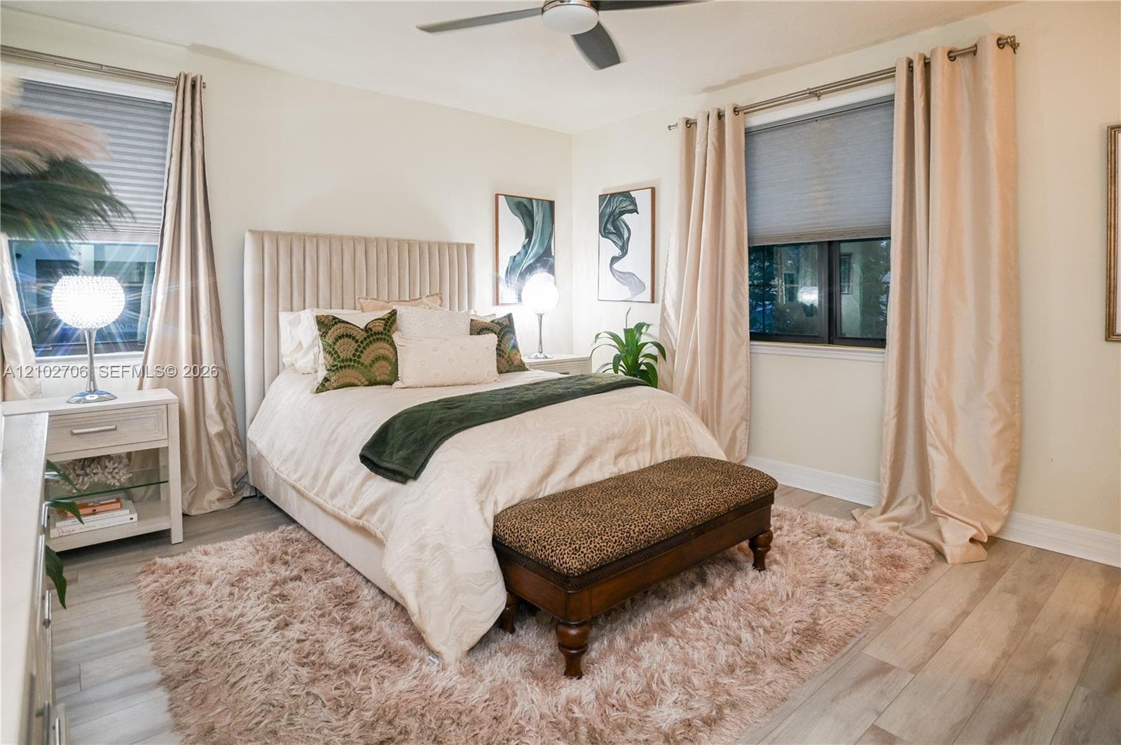 Neutral-toned bedroom featuring wood-finish flooring, a ceiling fan with integrated lighting, and dual windows